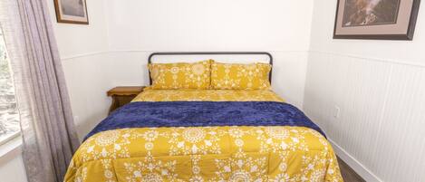 A bed with a floral bedspread, a dark blue throw blanket, and a wooden headboard.