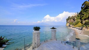 A seaside terrace with clear views of the ocean and a distant mountain, featuring stone pillars with plants. - Villa Sirenea: A splendid and luminous three-story villa located right on the beach, with Free WI-FI. (Vico Equense)