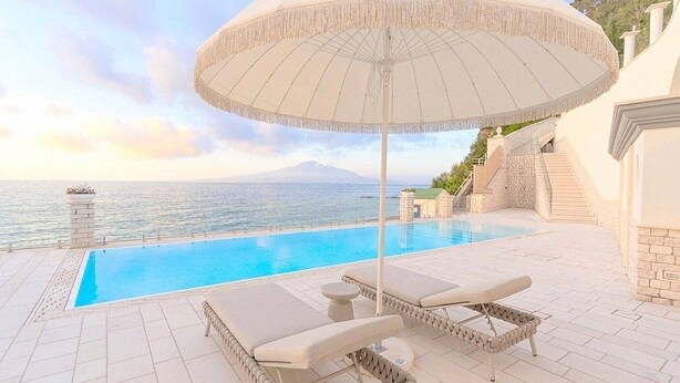 A poolside area with lounge chairs and an umbrella, overlooking a body of water and a mountain. - Villa Sirenea: A splendid and luminous three-story villa located right on the beach, with Free WI-FI. (Vico Equense)