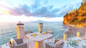 A terrace with a table and chairs, overlooking a beach and a mountain. - Villa Sirenea: A splendid and luminous three-story villa located right on the beach, with Free WI-FI. (Vico Equense)