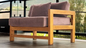 Une chaise en bois avec des coussins, placée sur un balcon offrant une vue sur les montagnes et les arbres.