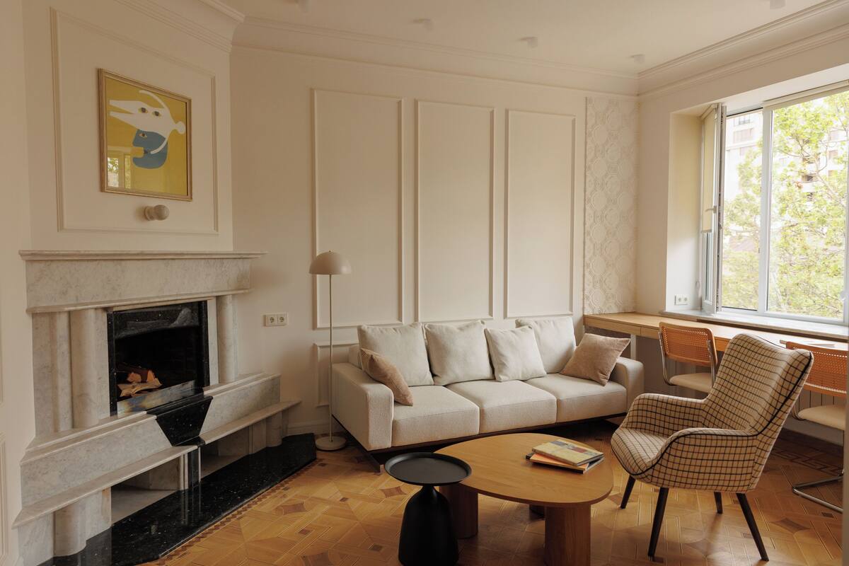 Una sala de estar con chimenea, sofá, sillón, mesa de centro y un ventanal grande.