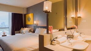 Una habitación de hotel con una cama grande, un baño con lavabo y espejo, y vistas a la ciudad.