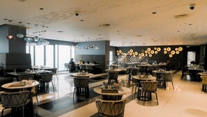 Un restaurante moderno con mesas redondas, sillas negras y una pared de lámparas circulares.