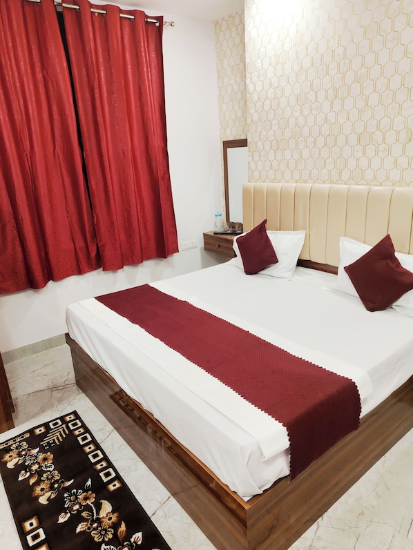 A hotel room with a bed, red curtains, a nightstand, a mirror, and a patterned wall. - Hotel Kashi Bliss (Varanasi)