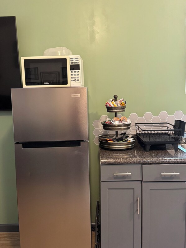A kitchen with a stainless steel refrigerator, a microwave, and a hexagonal tile backsplash.
