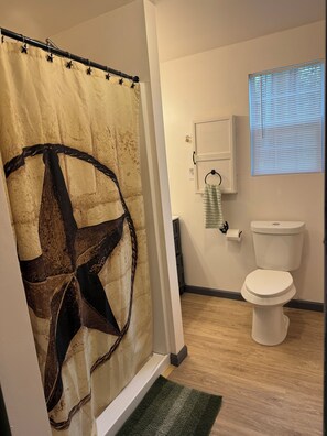 A bathroom with a shower curtain, a toilet, a towel rack, and a window with blinds.