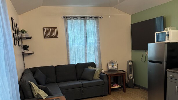Ein gemütlicher, kleiner Wohnraum mit Deckenventilator, einer Couch, einem kleinen Tisch, einem Fernseher und einem Kühlschrank.