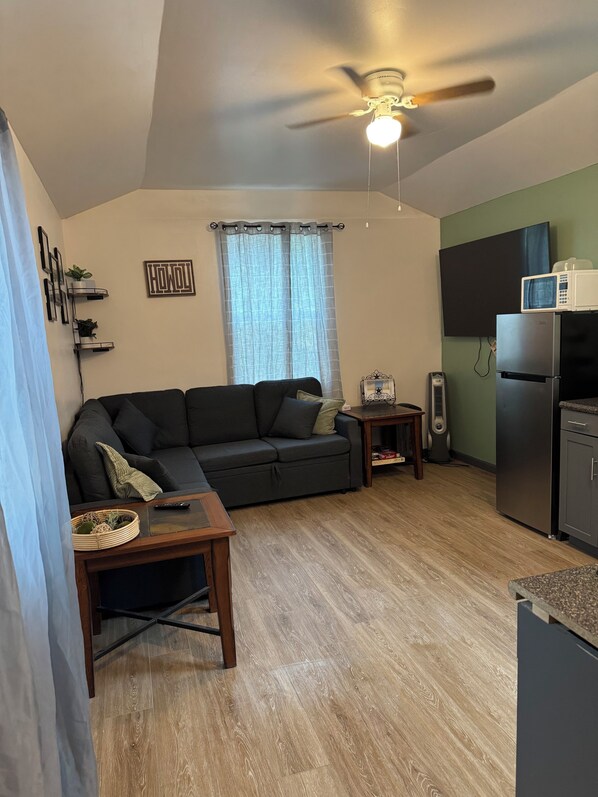 A compact living space with a ceiling fan, a sofa, a small table, a TV, and a refrigerator.