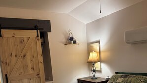 Ein Schlafzimmer mit Holztür, einem Bett mit einem gemusterten Quilt, einer Nachttischlampe und einer Wandklimaanlage.