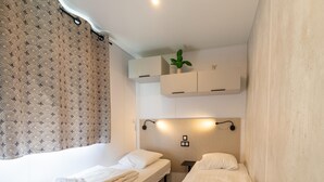 Een kleine, schone kamer met twee bedden, een nachtkastje, een wandplank met een plant en een wandlamp.