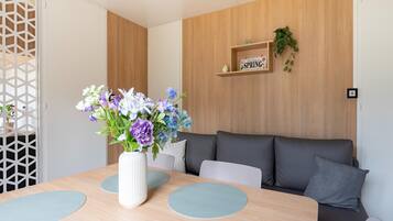 A modern living room with a wooden accent wall, a sofa, a dining table with a vase of flowers, and a shelf with a sign.