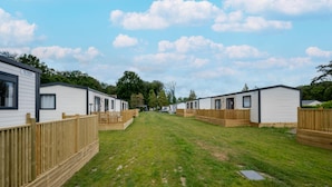 A row of mobile homes with a grassy yard and wooden fences. - Charming Caravan With Terrace for 6 (Kaprijke)