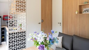 A modern room with a wooden door, a white partition with a geometric pattern, a grey sofa, and a small shelf with a sign. - Charming Caravan With Terrace for 6 (Kaprijke)
