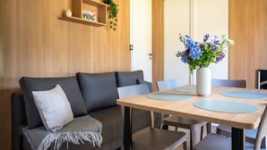 Een moderne woonkamer met een bank, een eettafel met stoelen, een vaas met bloemen en een houten plank met een bord.