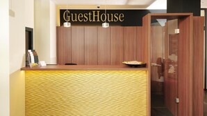 A reception desk with a 'GuestHouse' sign, a wooden counter, and a glass door leading to a room. - GuestHouse Mainz (Mainz)