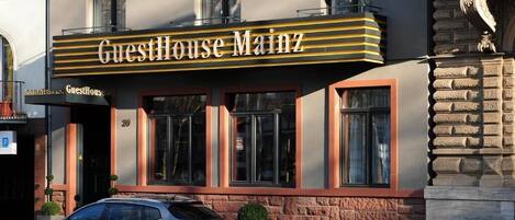 Un edificio con un letrero que dice 'GuestHouse Mainz' y un coche estacionado adelante.