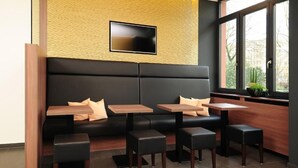 A modern seating area with a black sofa, wooden tables, and black stools. - GuestHouse Mainz (Mainz)