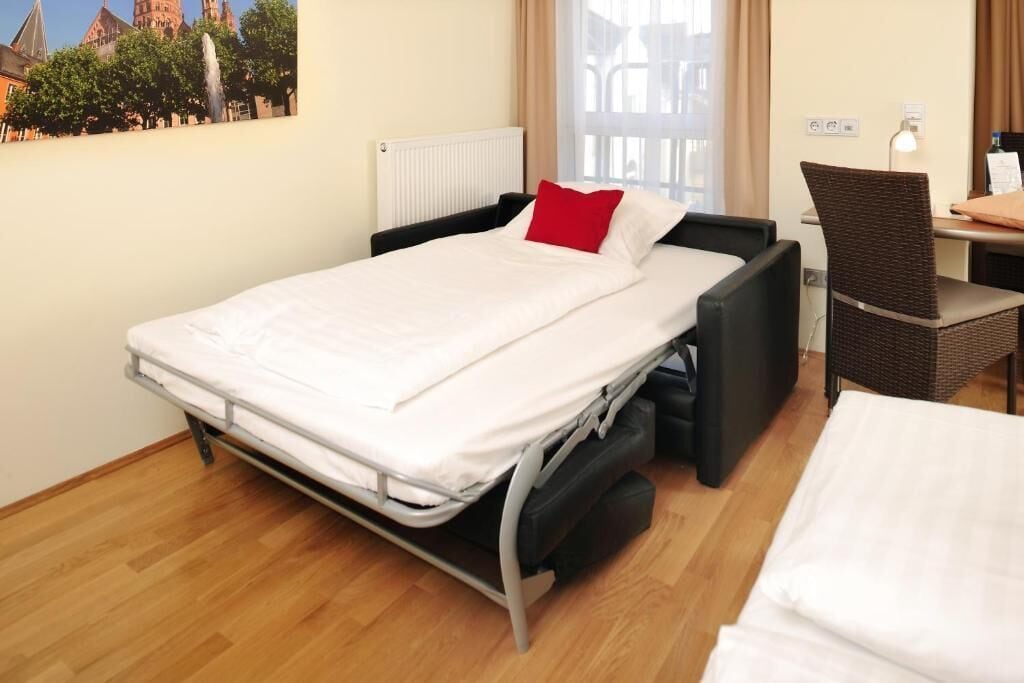 Habitación de hotel con cama, una silla, un escritorio y vista a un edificio.