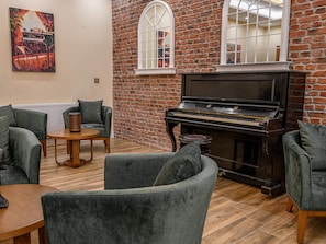 A room with a piano, brick wall, and grey upholstered chairs. - 2 Person Holiday Park Home in Erlbach (Markneukirchen)