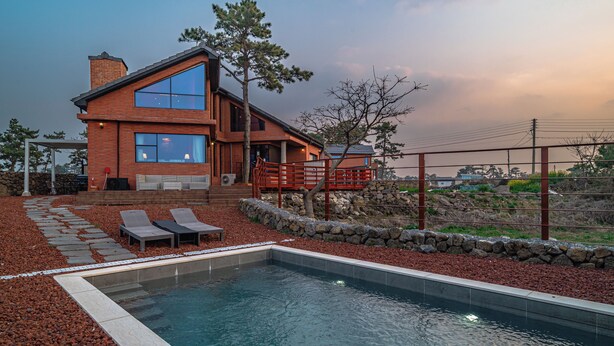 A modern house with a swimming pool, stone pathway, and a wooden deck with chairs.