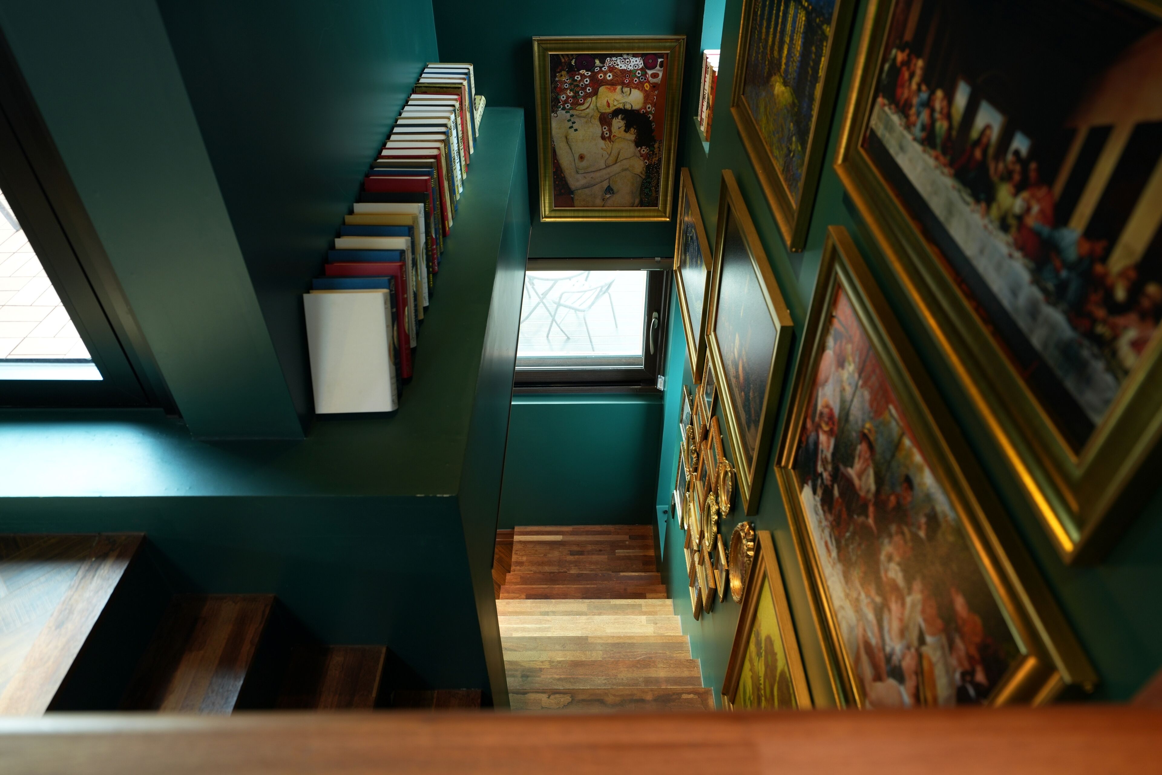 Eine Treppe führt zu einem Raum mit Bücherregal, gerahmten Bildern und einem Fenster.