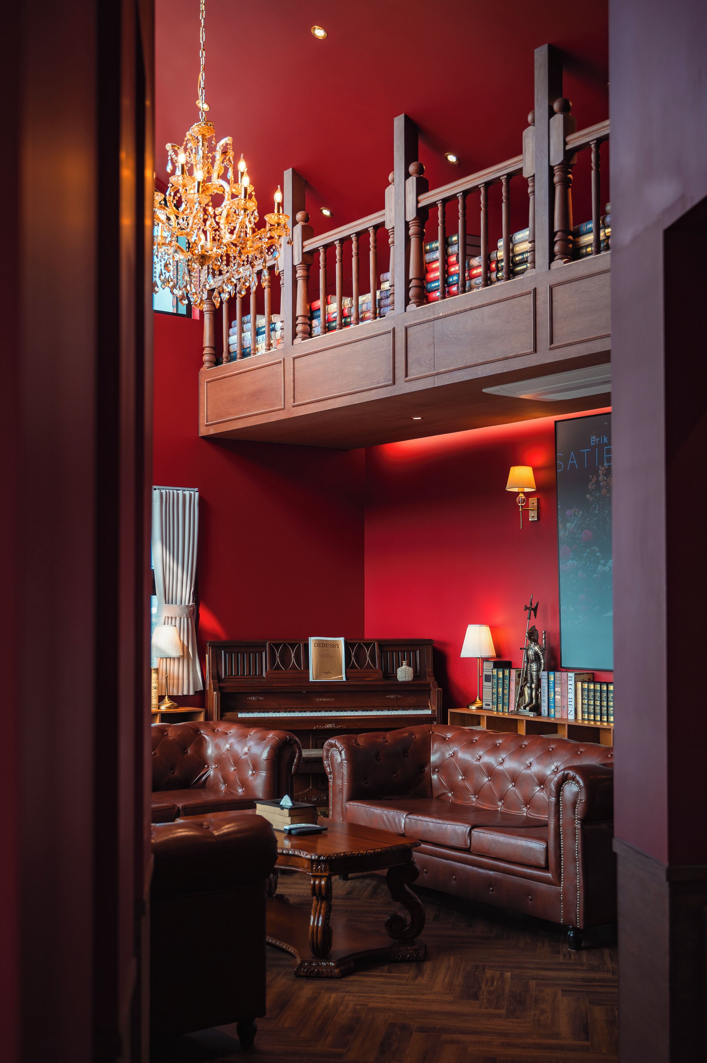 Una habitación con una pared roja, una araña, un piano, un sofá y una estantería.