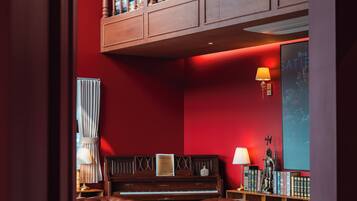 Una habitación con una pared roja, una araña, un piano, un sofá y una estantería.