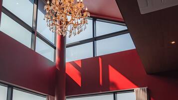 A modern interior with a large chandelier, leather sofas, and a piano.