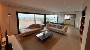 Una sala de estar moderna con un ventanal grande, un sofá, una mesa de centro y una cocina al fondo.