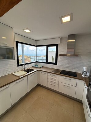 Eine moderne Küche mit großem Fenster, weißen Schränken und Blick auf eine Küstenstadt.