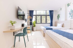 Una habitación de hotel moderna con una cama, un escritorio con silla, un televisor montado en la pared y una ventana con cortinas.