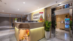 A hotel reception desk with a Christmas tree decoration, a digital screen, and a refrigerator stocked with beverages. - Bin Bin Hotel 18 - Near Thu Thiem Villa Park (Ho Chi Minh City)