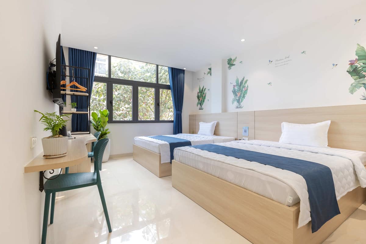 Ein Hotelzimmer mit einem Bett, zwei Nachttischen, einem Schreibtisch mit Stuhl, einem an der Wand befestigten Fernseher und einem Fenster mit Vorhängen.