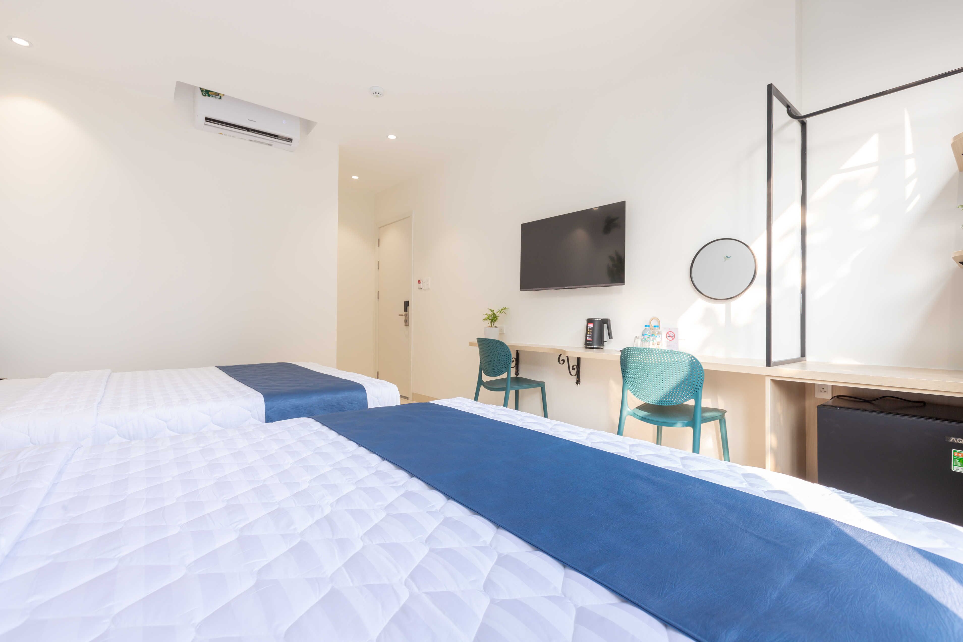 Una habitación de hotel con dos camas, un escritorio, una silla, un televisor, un espejo y un aire acondicionado.