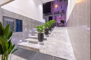 Vestíbulo de hotel con una escalera, plantas en macetas y un cartel sobre la escalera.