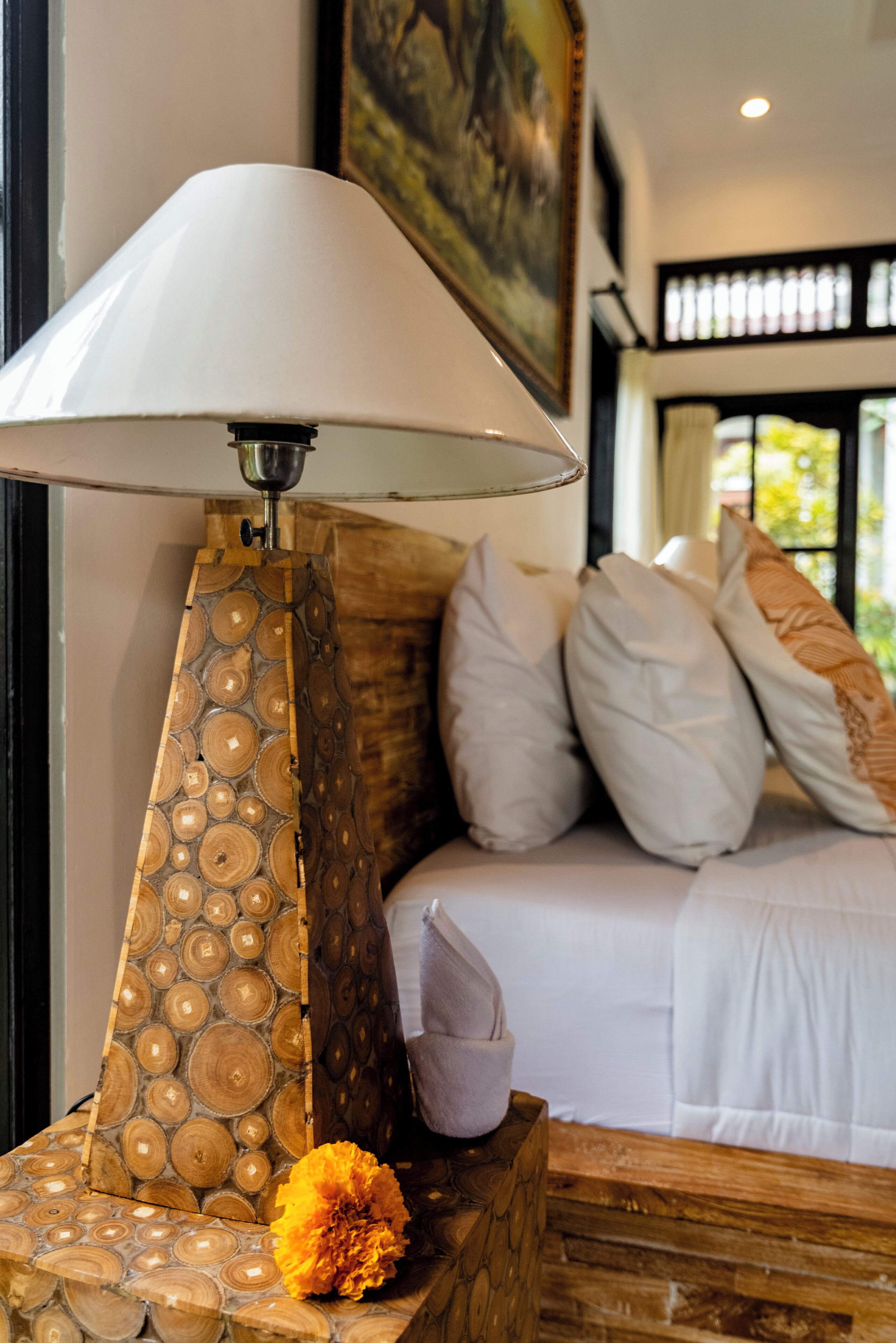 Una cama con ropa blanca, una mesita de noche de madera con una lámpara y un panel decorativo de madera.