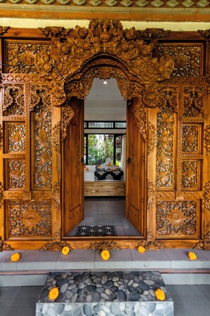 An ornate wooden doorway with intricate carvings, leading to a room with a bed and a view of greenery outside. - Clement Ubud by Dhananjaya hospitality (Sebatu)