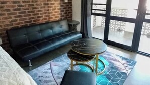 A room with a brick wall, a black sofa, a round table, and a large window with a view.