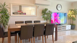 A modern living room with a dining table, chairs, a flat-screen TV, a clock, and potted plants. - Spacious 4BR Family Home, 5 Min to Rockingham Foreshore (Rockingham)