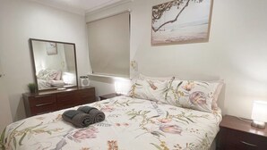 A bedroom with a bed, a bedside table, a mirror, a ceiling fan, and a painting on the wall. - Spacious 4BR Family Home, 5 Min to Rockingham Foreshore (Rockingham)