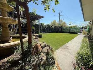 A well-maintained garden with a stone fountain, a paved pathway, and a neatly trimmed lawn.