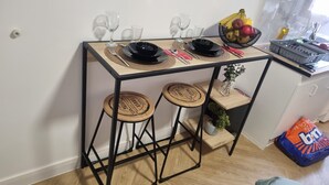 Una mesa de comedor con taburetes, una cesta de fruta y una zona de cocina con una bolsa de papas.