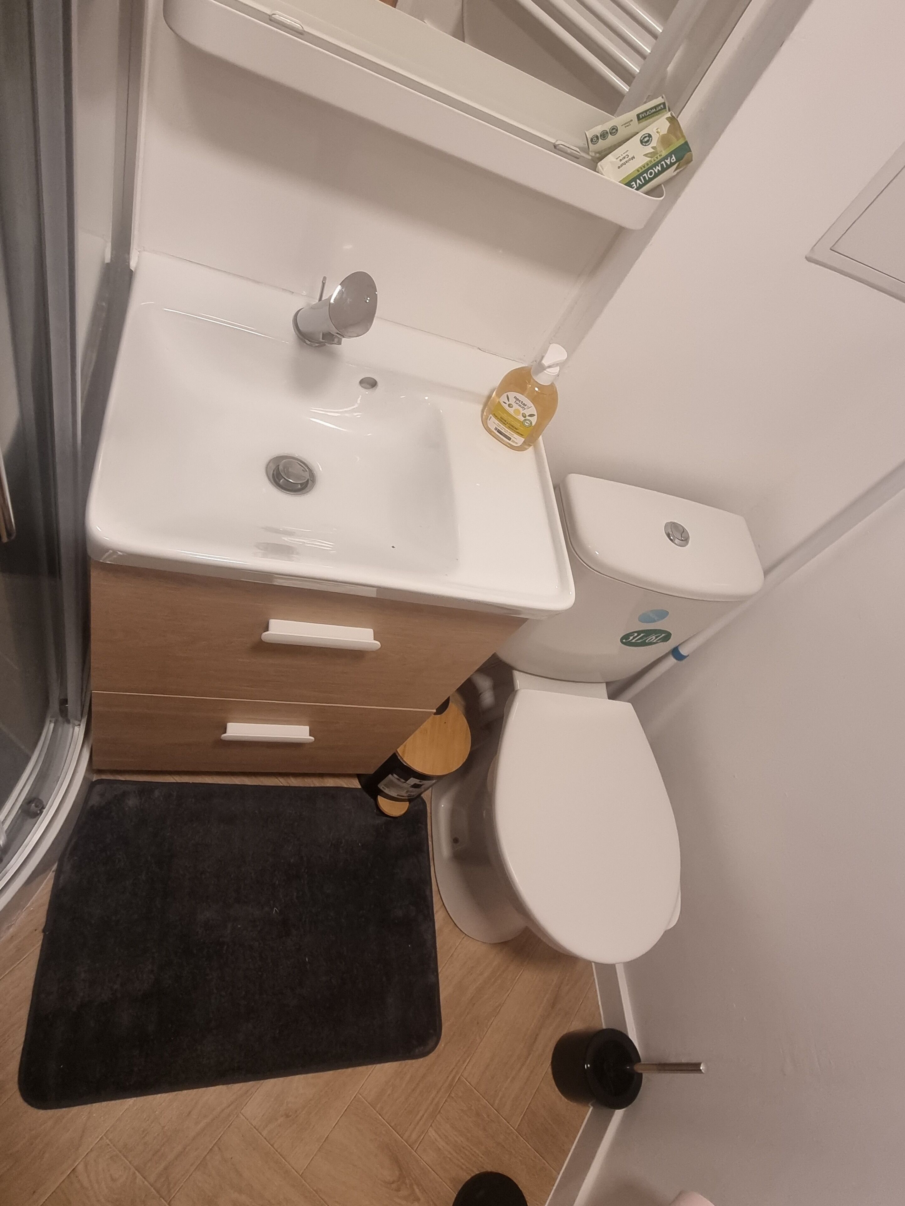 A bathroom with a white sink, toilet, and a black mat.