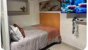 Een slaapkamer met een bed, een televisie, een plank met bloemen en een kunstwerk aan de muur.