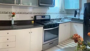 Een moderne keuken met witte kasten, een roestvrijstalen fornuis, een magnetron en een zwarte koelkast.