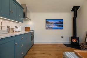 A modern kitchen with teal cabinets, a stove, and a painting of a mountain landscape. - Beautiful One BD Cottage Near Burford (Burford)