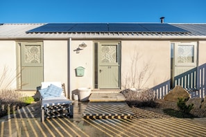 A building with a solar panel roof, a front door, a mailbox, a bench, and a small garden area. - Beautiful One BD Cottage Near Burford (Burford)