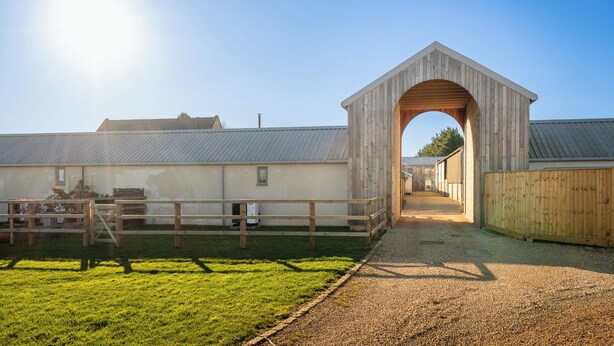 A barn with a wooden archway, a gravel path, and a fenced area. - Beautiful One BD Cottage Near Burford (Burford)