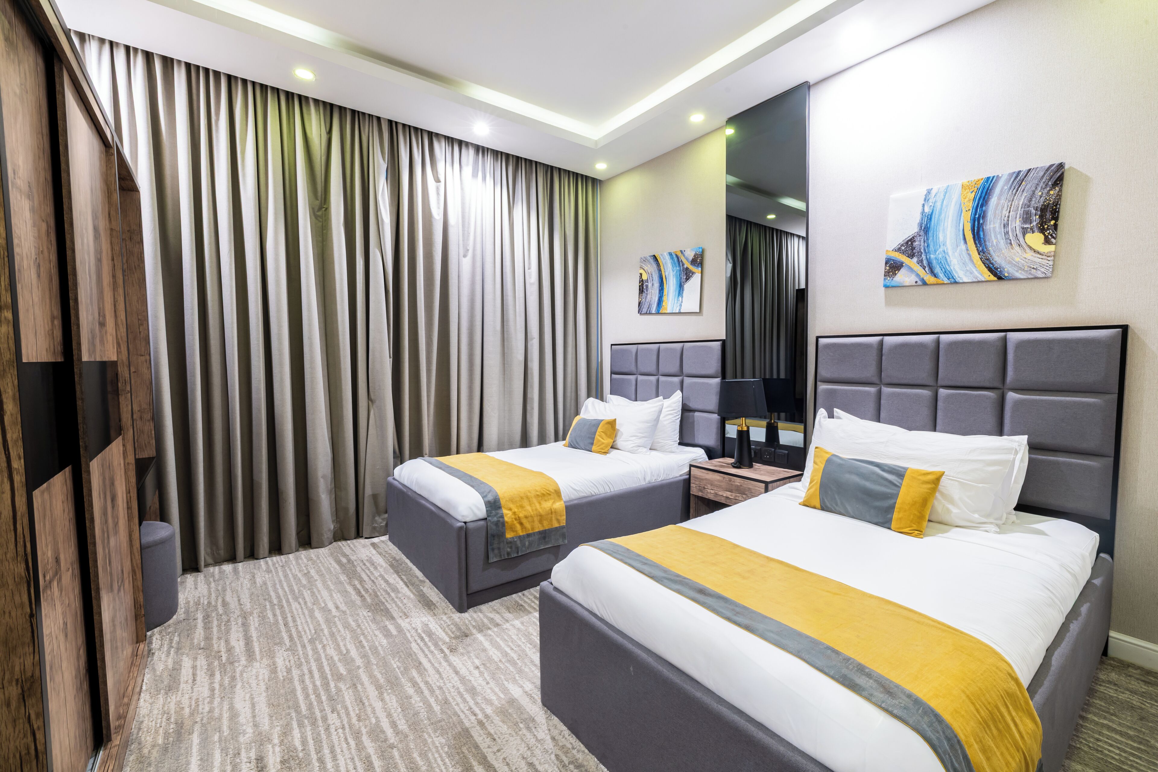 A hotel room with two beds, a large window with curtains, a flat-screen TV, and a painting on the wall.